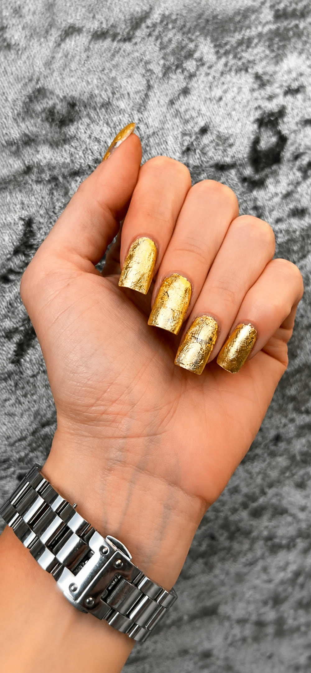 Gold chrome manicure catching the light, worn with a silver watch.