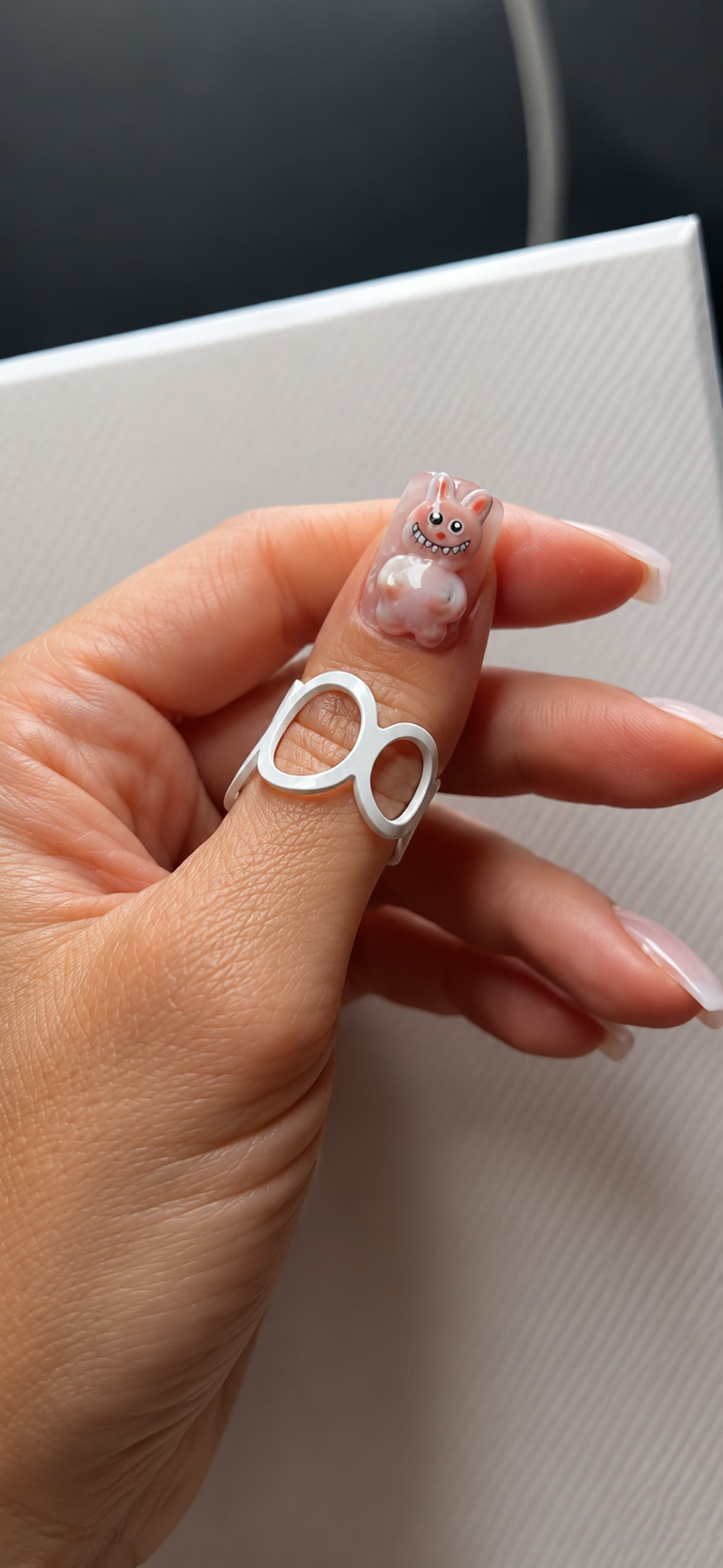 Milky pink nails holding a fine silver ring.