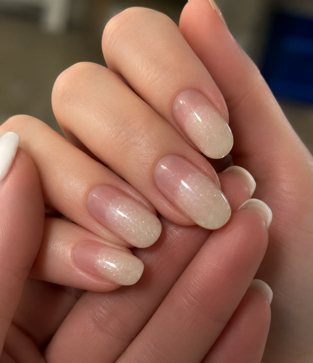 Glossy milky-nude almond nails, both hands resting together.