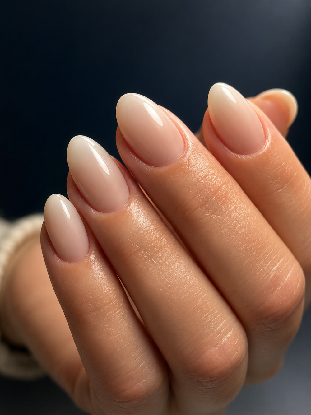 Milky nude almond nails in soft light against a dark background.