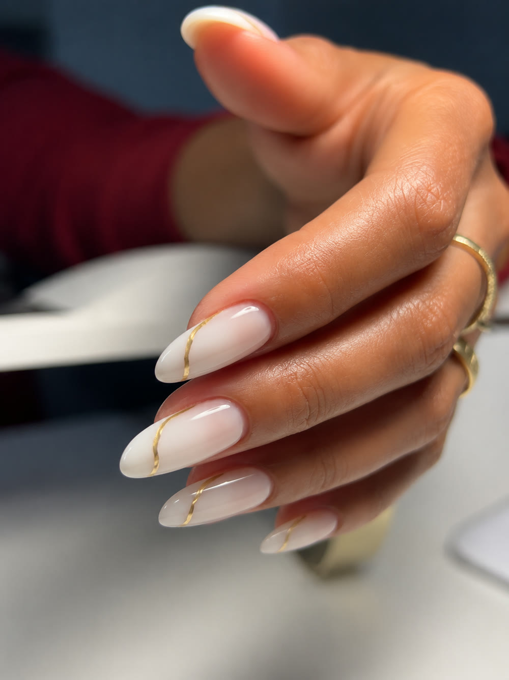 Milky white nails traced with a fine gold line, worn with a gold ring.